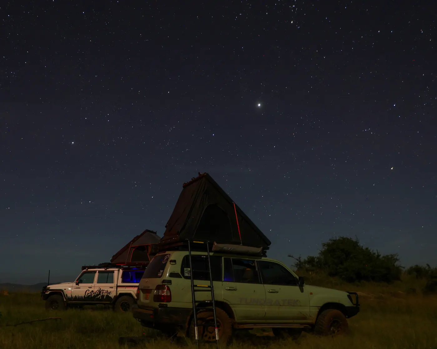 Two parked expedition vehicles with rooftop tents beneath a star-filled sky