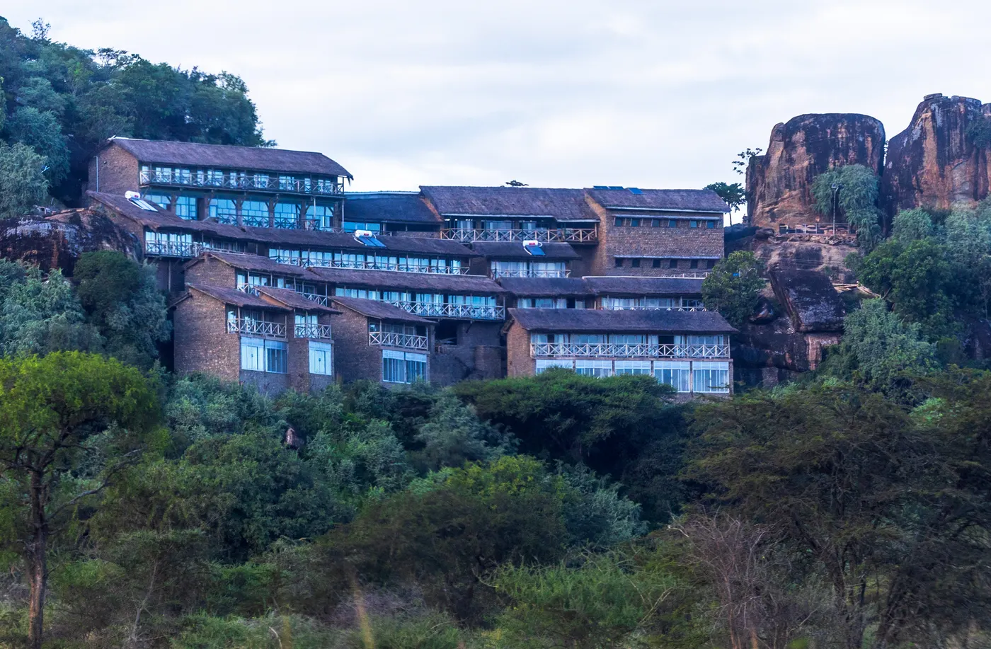 Building tucked against a rocky hillside above trees