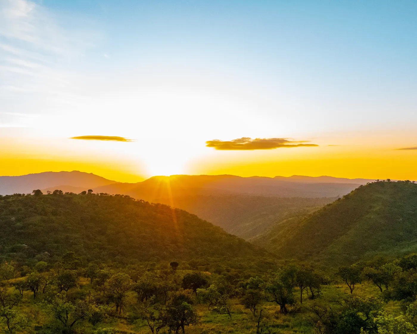 Sun rising over a succession of green hills and valleys