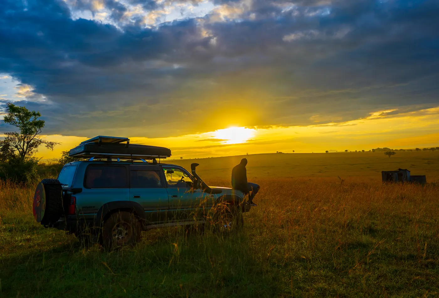 Expedition vehicle parked in open grassland at sunset with a person nearby