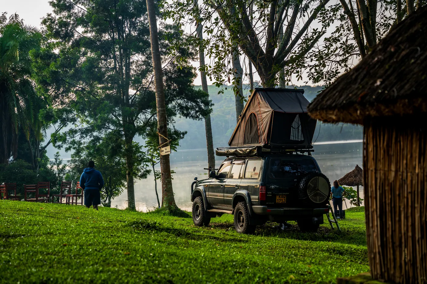 Expedition vehicle with a rooftop tent beside water and trees