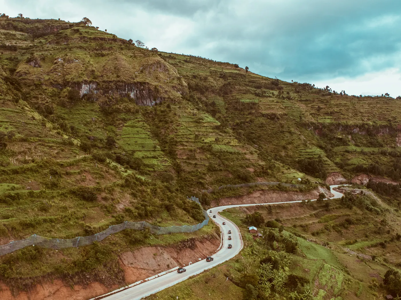 Aerial view of a road curving across green hills with vehicles along it