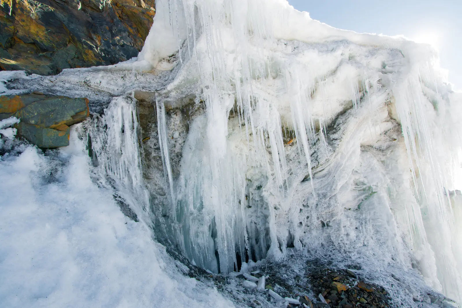 Ice and long icicles hanging over dark mountain rock