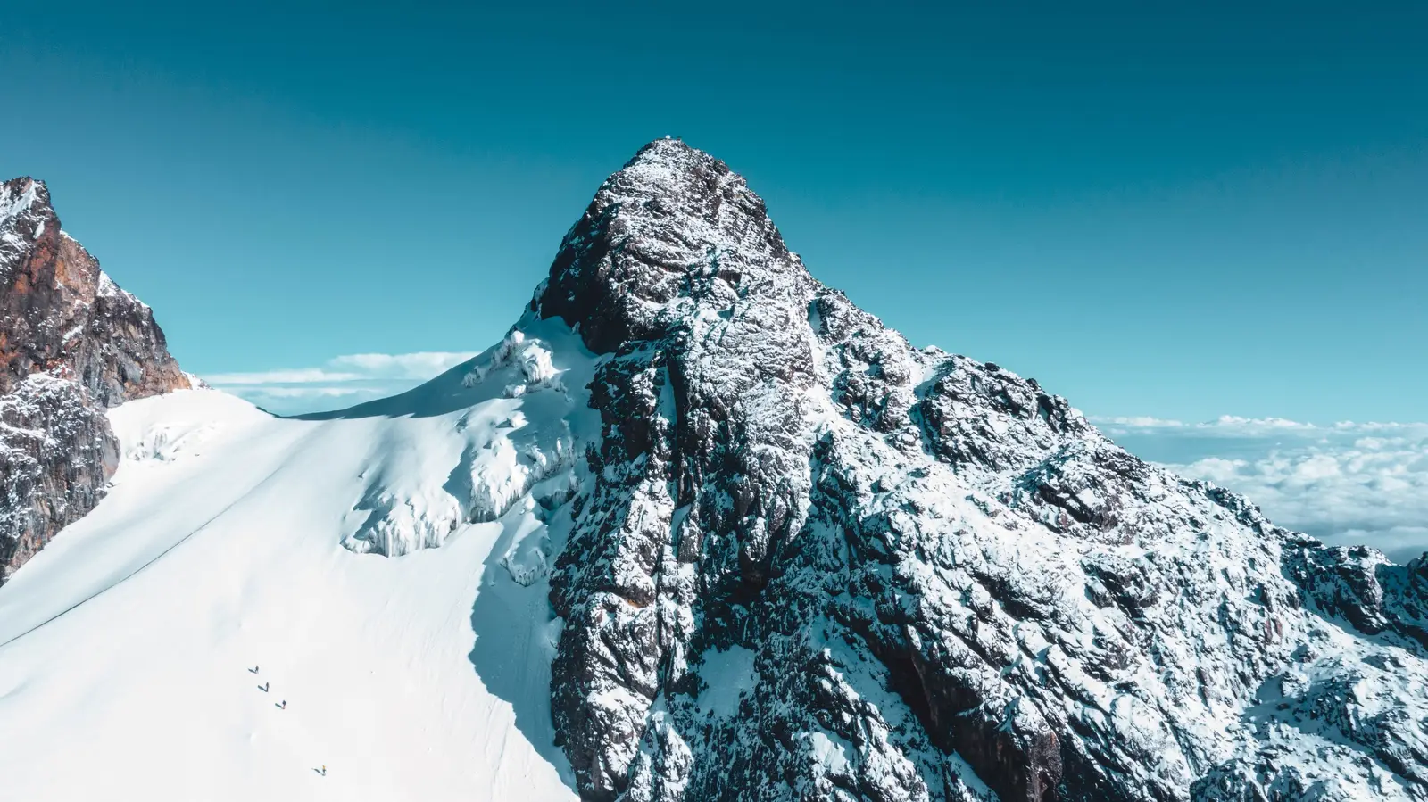 Steep snow-covered mountain peak above a bank of clouds